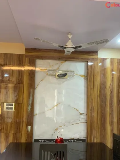 A view of a dining area where we combined a simple false ceiling with a feature wall. The wall combines high-gloss wood-finish panels with a central marble-effect panel, demonstrating our skill in handling multiple materials.