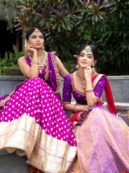 A dual model shoot featuring complementary lehengas in shades of purple and magenta. This type of shot is perfect for showcasing a designer's collection, highlighting how different pieces work together.