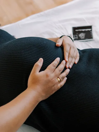 A close-up detail shot focusing on the mother's hands on her belly, with the first ultrasound photo nearby. It’s these small details that hold so much meaning in your pregnancy journey.