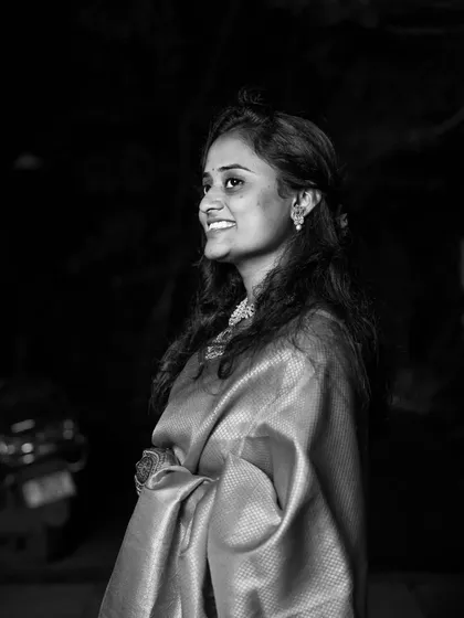 A beautiful black and white portrait capturing a shy, downward glance and a gentle smile, highlighting the elegance of the saree.