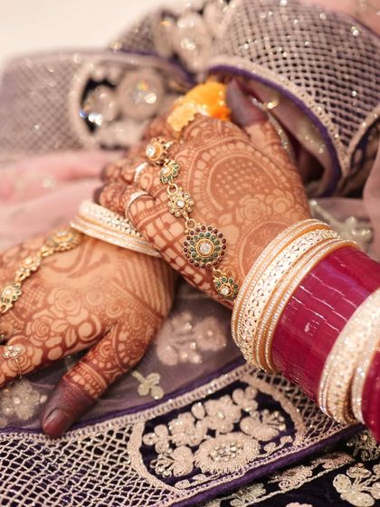 A professional shot capturing the rich, dark stain of the henna against the bride's beautiful jewelry and outfit. The color is consistent and deep across both hands.