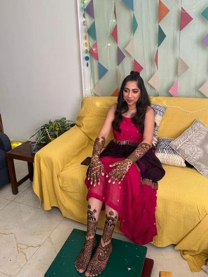 A full-length view of the bride during her mehndi application, showing the complete design on her hands and feet.