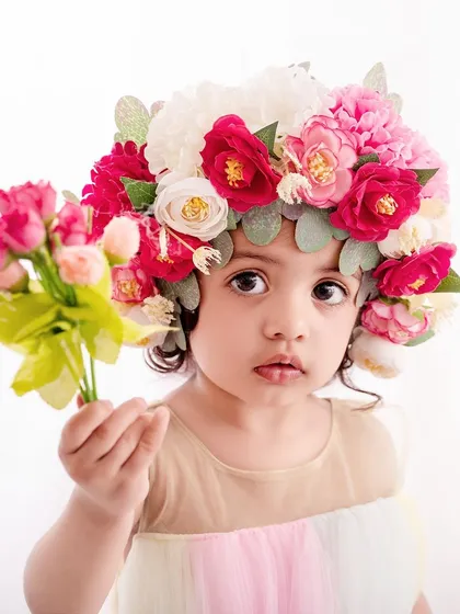A unique and artistic portrait, this little girl wears a magnificent crown of flowers, looking like a true queen of the garden.