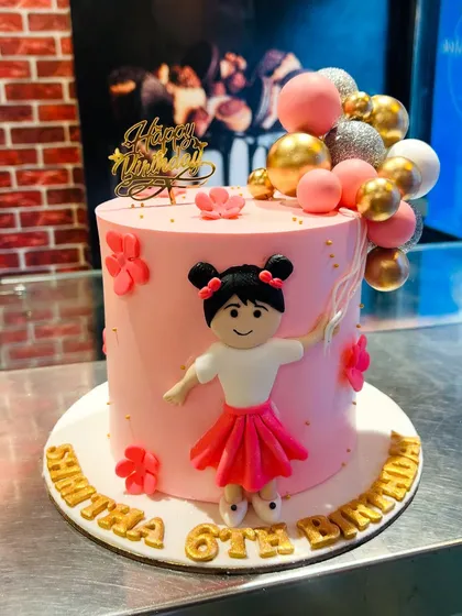 A charming pink cake with a fondant girl figurine holding a bouquet of balloons for a 6th birthday.