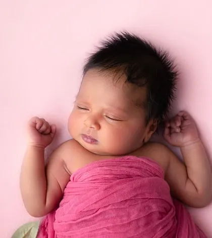A sleepy yawn from a three-week-old baby wrapped in a vibrant pink swaddle. This candid moment captures the real, unposed sweetness of the newborn phase.