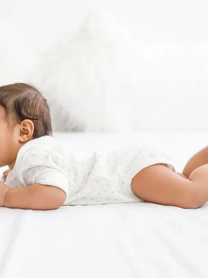 Giggles and wiggles on a comfy white bed. The simple, bright setup allows the baby's joyful energy to be the star of the photo.