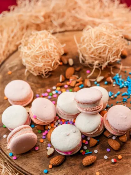 Another beautiful shot of our pink and white macarons, scattered with almonds and colorful sprinkles on a wooden board.