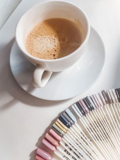 This is the lifestyle my courses can help you build. An aesthetic shot of coffee next to a wide array of nail color swatches, representing the creative world of a professional nail technician.