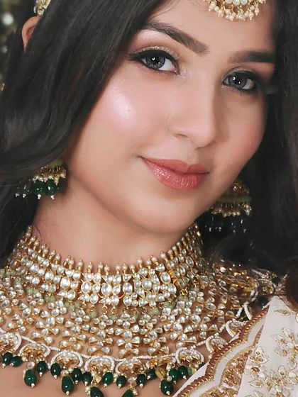 A close-up of a beautiful multi-layered Kundan necklace with green bead drops, paired with a white and gold outfit.