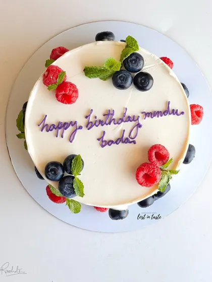 A simple yet beautiful celebration cake with chocolate buttercream, decorated with fresh raspberries, blueberries, and mint leaves for a pop of color and flavor.