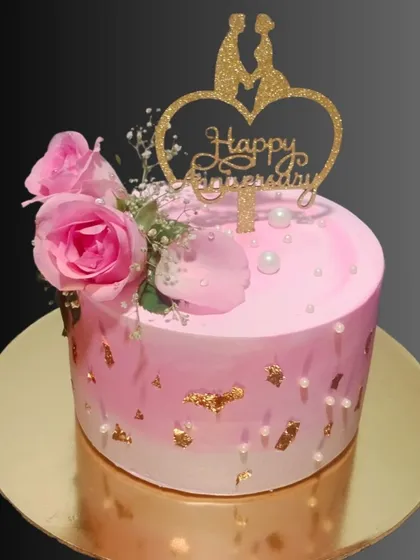 A beautiful pink anniversary cake decorated with fresh roses and gold leaf flakes. The heart-shaped topper makes it a romantic centerpiece for celebrating your love.