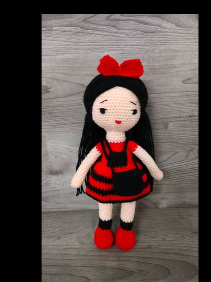 A very cute doll in a red and black dress with a big red bow in her hair.