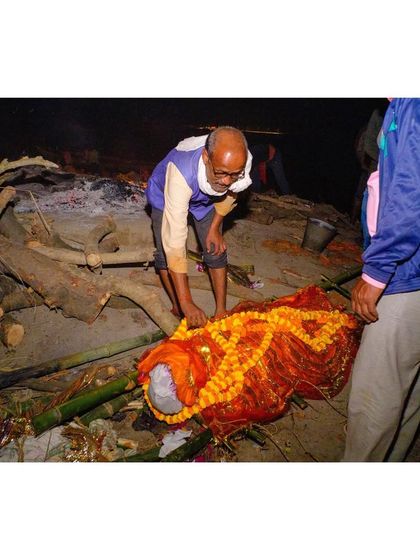 A body wrapped in orange cloth and adorned with marigold garlands is prepared for the last rites.