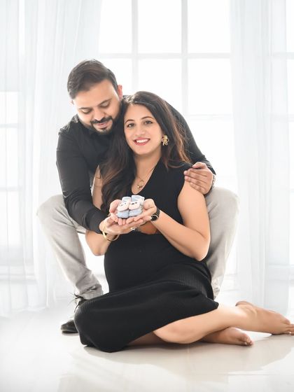 A sweet and simple couple's portrait. Seated on the floor in our minimalist studio, they hold a pair of tiny baby shoes, a perfect prop to announce their excitement.