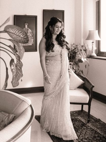 A beautiful sepia-toned portrait of the bride in her sparkling saree. The soft light from the window and the classic decor create a timeless, gentle image full of quiet anticipation.