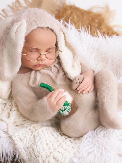 An adorable baby dressed in a fluffy bunny costume with round glasses, holding a tiny coffee cup for a quirky and cute portrait.