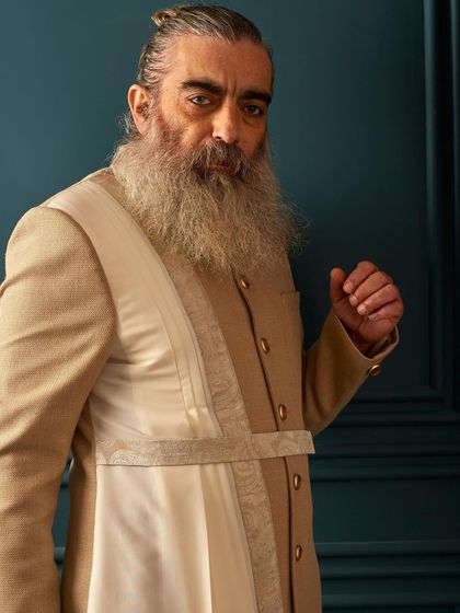 A close-up view of the beige draped sherwani, showing the texture of the fabric and the clean, buttoned front. This is understated elegance at its best.