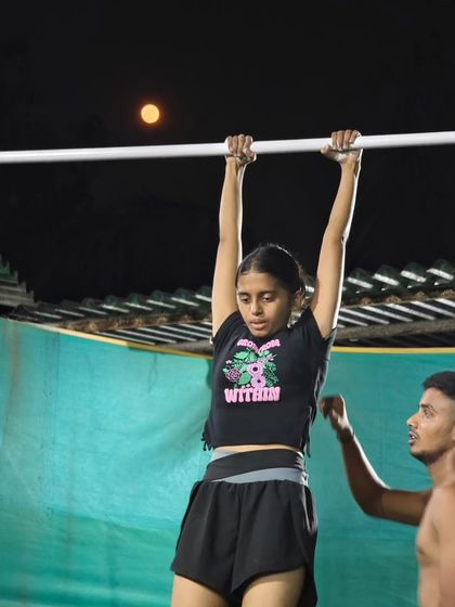 A coach providing support during a pull-up session under the moon. We are here to guide our athletes every step of the way.