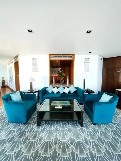 A seating arrangement in the Intercontinental Mumbai suite, showcasing the plush teal velvet armchairs and sofa. The geometric-patterned rug adds a contemporary touch to the elegant space.