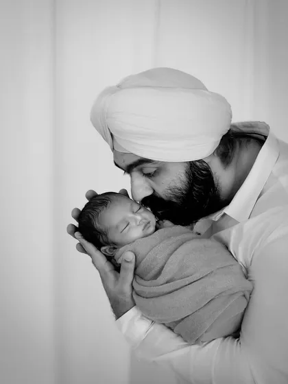 A black and white portrait of a father kissing his newborn's forehead. The monochrome tones add a timeless, emotional quality to this incredibly tender moment.
