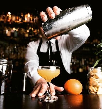 A professional bartender meticulously pouring a cocktail at a private house party. Hiring a professional ensures you can relax and enjoy your own event while your guests receive top-tier service.
