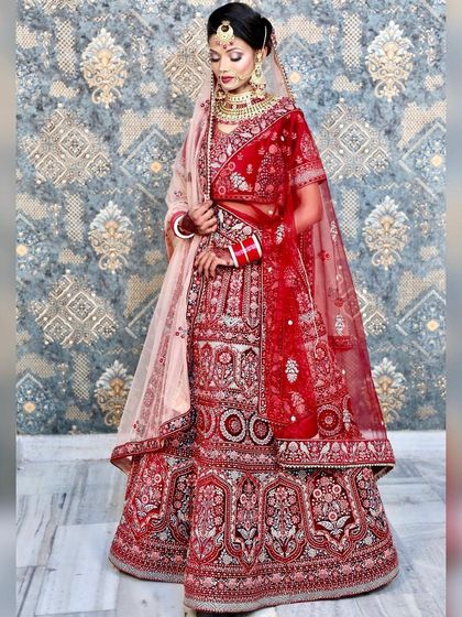 A full-length studio shot of a classic red bridal lehenga. The peach-colored dupatta adds a soft, modern contrast to the traditional red, offering a unique styling option.