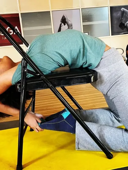 A student holds a deep backbend over a yoga chair. This prop is specifically designed to support the spine, allowing for a safe and therapeutic opening of the chest and shoulders.