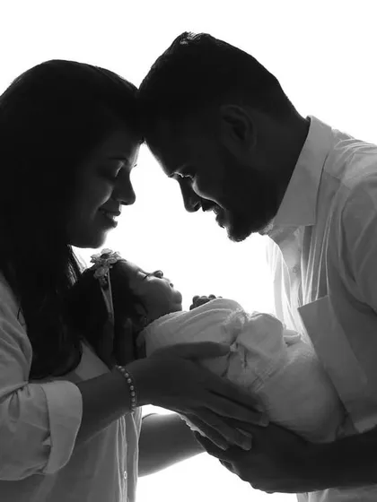 A silhouette of a family of three, their heads bowed together over the newborn, creating a circle of love.