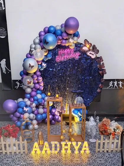 A dazzling birthday setup with a dark blue sequin backdrop. The crescent-shaped balloon garland and butterfly accents add a touch of magic, while the light-up letters personalize the space.
