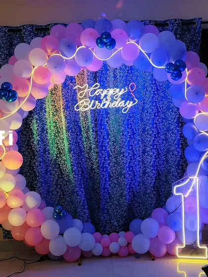 A simple yet elegant first birthday setup with a pink and blue balloon circle and a leafy backdrop.