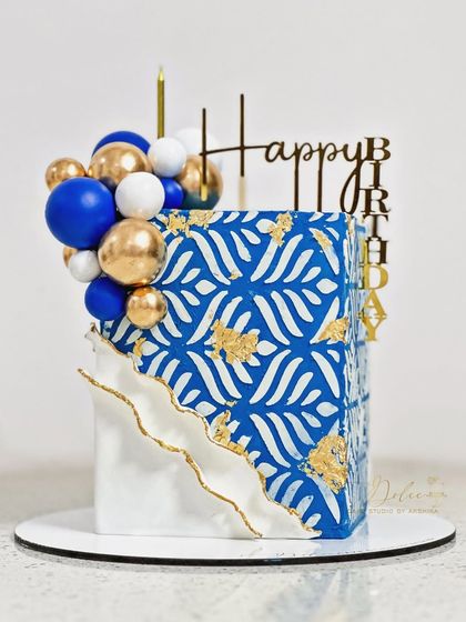 Not your regular birthday cake. This square cake features a bold blue and white stencil pattern with gold leaf accents and a cluster of balloons.
