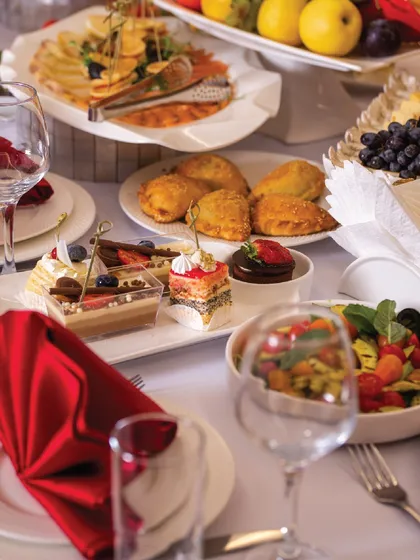 An invitation to indulgence. A table laden with our finest delicacies, from savoury pastries to fresh salads and decadent desserts, creating a complete sensory experience.