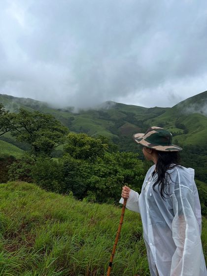 A trekker in a camo hat looks out over the vast green expanse of the Netravathi landscape.
