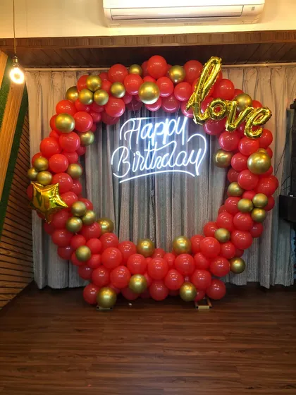 A custom birthday backdrop designed for a client in Mumbai. The circular balloon arch in red and gold, paired with a 'Happy Birthday' neon sign and a 'love' foil balloon, creates a perfect spot for celebration photos.