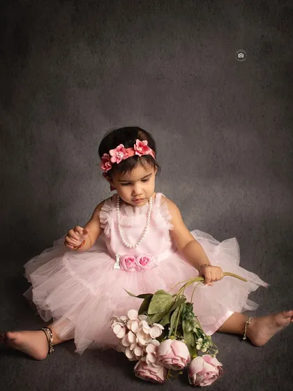 A sweet and simple portrait of a birthday girl in a pink dress, sitting with a bouquet of flowers against a classic grey backdrop.