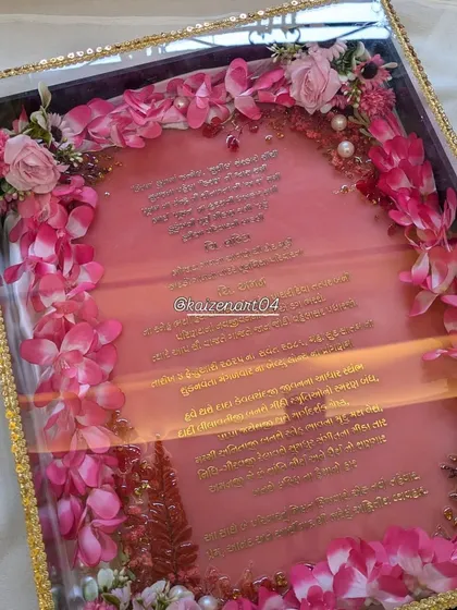 A high-quality image of the pink resin wedding invitation, showing the intricate Gujarati font in metal stickers and the beautiful floral border.
