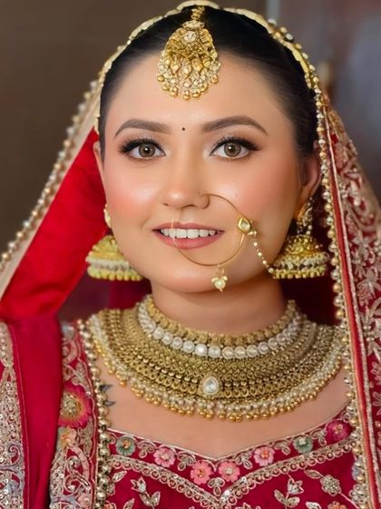 A close-up portrait of a smiling bride. Her makeup is natural and radiant, with a classic winged liner and a simple nath that enhances her features.