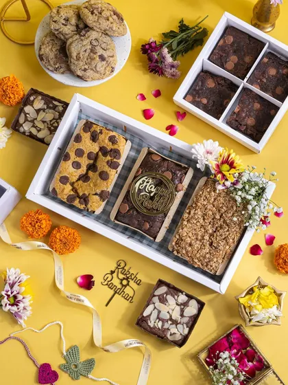 A flatlay of a beautiful Raksha Bandhan hamper filled with brownies, blondies, and cookies. I scattered flower petals and used a bright yellow background to give it a cheerful, celebratory vibe.
