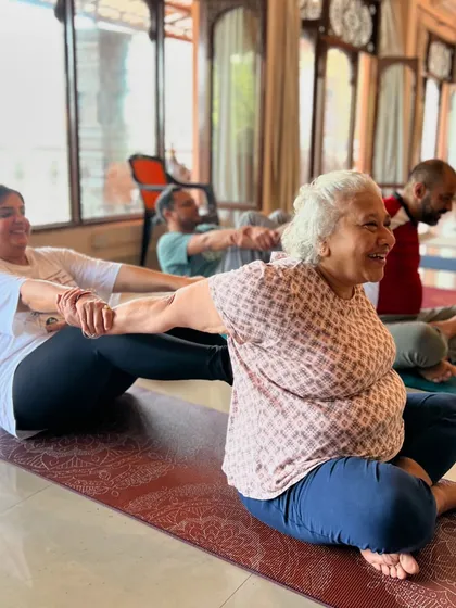 The spirit of our sangha, or community, is built on helping one another. Here, students of all ages, including a joyful senior practitioner, engage in partner yoga, sharing support and laughter. This shows that yoga truly is for everyone.