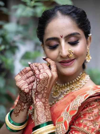 A close-up on the bride's happy face and beautiful henna, perfectly accessorized with a nath and gold jewelry to match the saree.