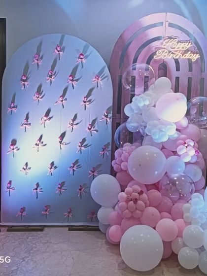 A delicate and modern pink-themed birthday setup. The decoration features two arched backdrops with different textures and a soft arrangement of pink and white balloons.