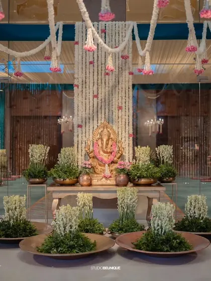 The main Ganesha setup at the entrance, surrounded by floral arrangements and traditional brass urlis. This creates a serene and divine welcome area.