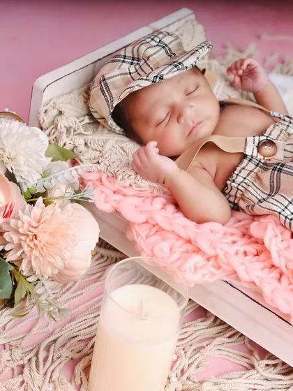 A close-up on the sleeping baby boy in his charming plaid outfit, highlighting his peaceful expression and the soft textures of the setup.
