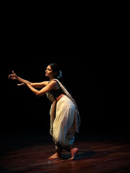 A dancer extends her arms in a gesture of offering during a Bharatanatyam performance.