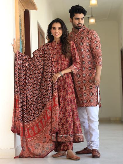 A geometric printed couple's outfit in a beautiful shade of red. The woman's Anarkali comes as a complete set with a bottom and dupatta.