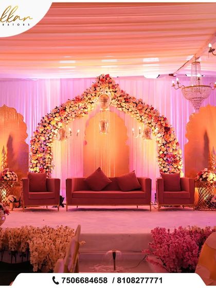A stunning reception stage with a floral arch in shades of pink and orange. The design, featuring chandeliers and elegant seating, creates a warm and majestic atmosphere.