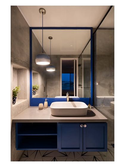 A modern bathroom design featuring a bold blue vanity and mirror frame against industrial polished concrete (IPS) walls. The geometric floor tiles add a graphic element to the space.