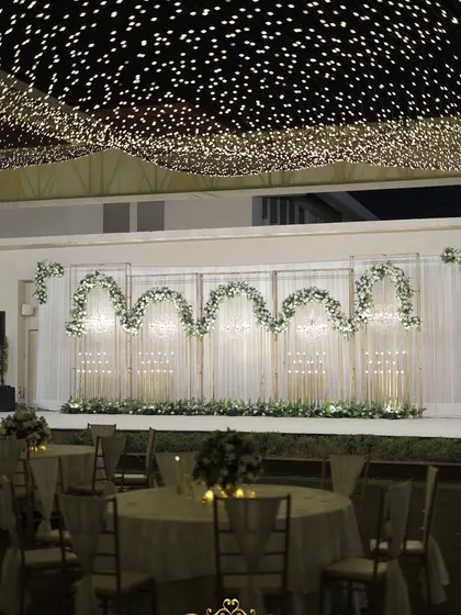 The main stage for the cocktail night, featuring a clean white backdrop with floral arches, set under a ceiling of twinkling fairy lights.