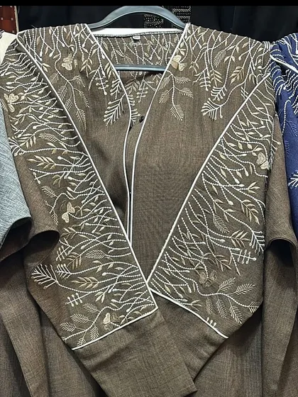 This brown abaya has a unique design with white piping and delicate branch embroidery. It's a sophisticated and earthy choice for modest wear.