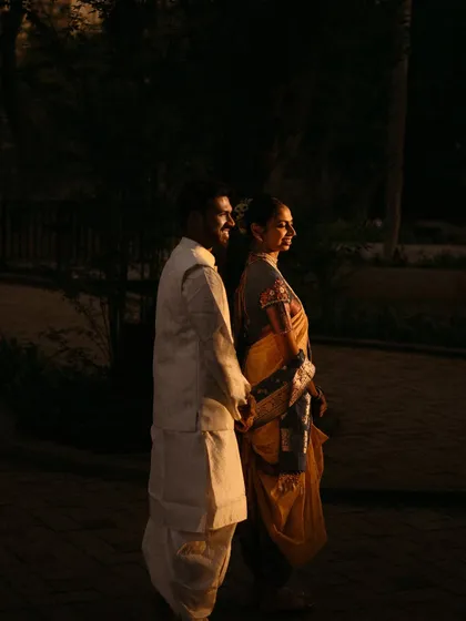 A dramatic shot of a couple in traditional wear, illuminated by a sliver of golden sunlight against a dark background.